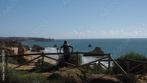 Mulher nova parada encostada a uma vedação olhando o mar azul. photo