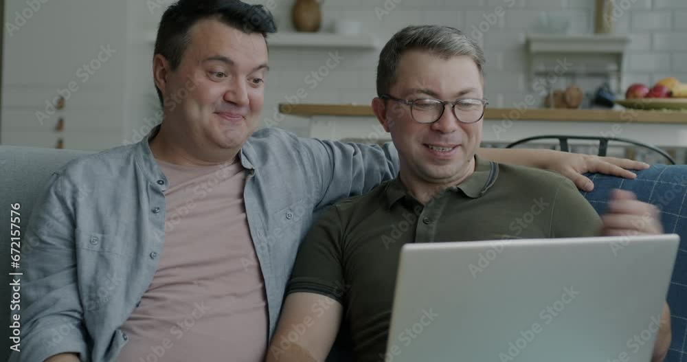 Two men happy gay couple making online video call with laptop talking showing thumbs-up discussing new house. Relocation and accommodation concept. Two men happy gay couple making online video call with laptop talking showing thumbs-up discussing new house. Relocation and accommodation concept.