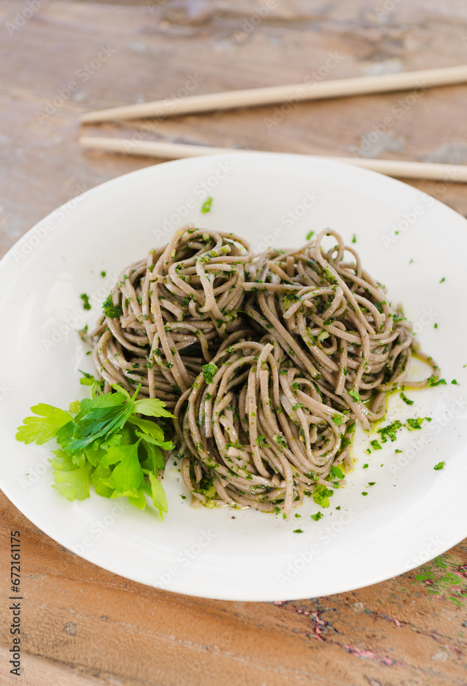 Organic brown noodles cooked in garlic oil, fresh coriander and sea salt. Served with chopsticks on a white plate.gourmet eating. Organic brown noodles cooked in garlic oil, fresh coriander and sea salt. Served with chopsticks on a white plate.gourmet eating.