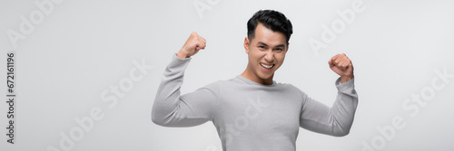 Obraz na płótnie Young handsome asian man over white backgroundshowing arms muscles smiling proud. w salonie