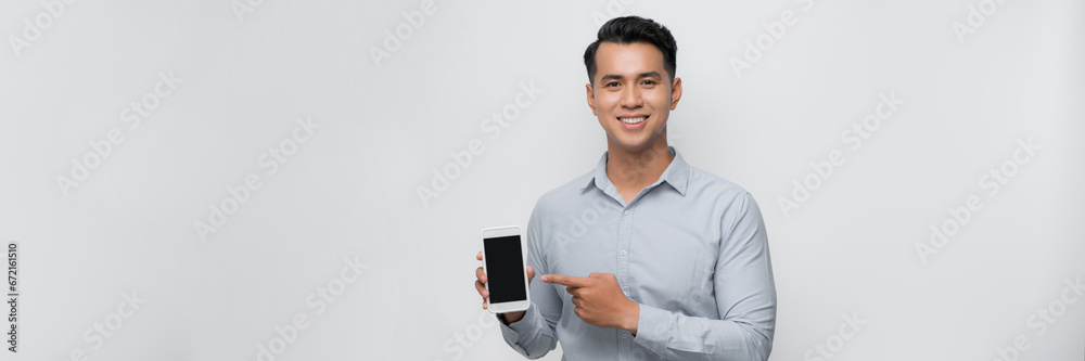 Smiling young man holds a modern smartphone in his hand and shows his finger on a blank screen
