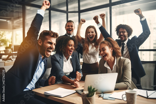 Happy diverse successful business team celebrating a triumph with arms up in startup office. Multiethnic business group with laptop screaming and holding fists up. photo