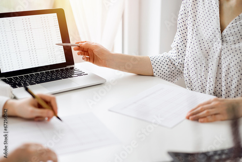 Two accountants using a laptop computer for counting taxes at white desk in office. Business Woman pointing into screen with a pen. Teamwork in business audit and finance
