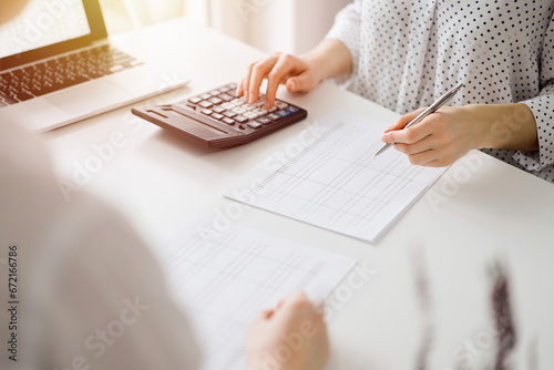 Accountant using a calculator and laptop computer for counting taxes with a client or a colleague at white desk in office. Teamwork in business audit and finance photo