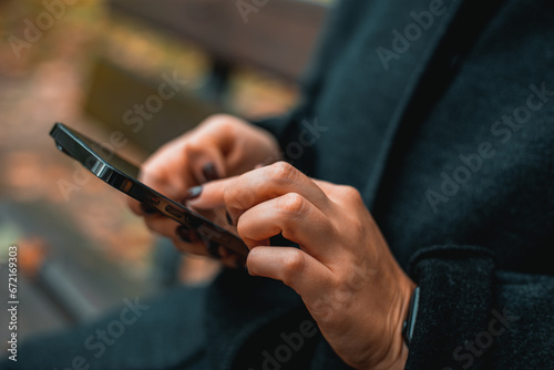 City lifestyle stylish using a phone texting on smartphone app in a street. Young woman with smartphone in hand close-up.