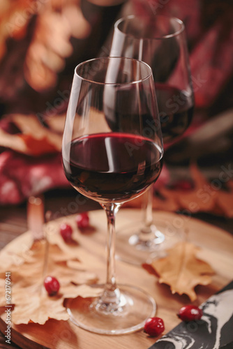 Autumn still life with two glasses of red wine and dry leaves in rustic style on dark wooden background. Romantic sweater weather concept