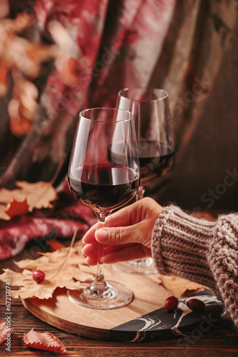 Autumn still life with two glasses of red wine and dry leaves in rustic style on dark wooden background. Womans hand holding glass. Romantic sweater weather  wine tasting concept