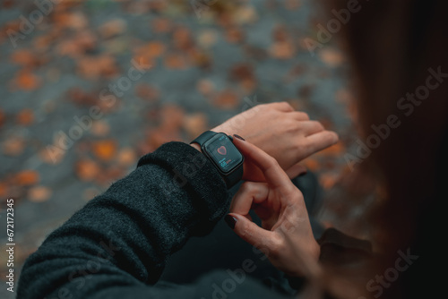 A woman watches her heart pulse on a smart watch while sitting on a bench in a park in autumn