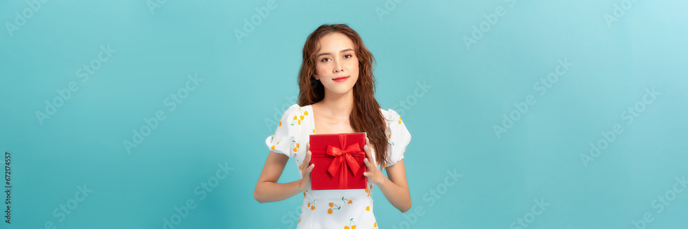 Portrait of a smiling young woman in summer dress holding gift box isolated over blue background Portrait of a smiling young woman in summer dress holding gift box isolated over blue background