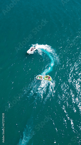 The speed boat carries a people in life jackets on the  boat on the blue sea. The view from the top. Aerial photo of extreme power boat donut water-sports cruising in high speed in Adriatic sea © Andrew