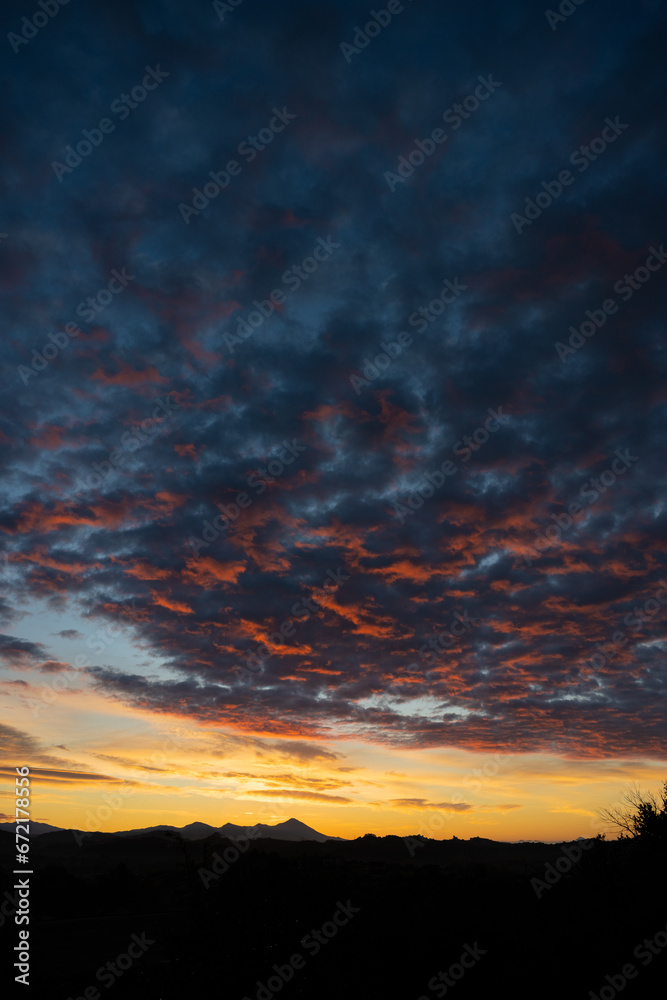 Stunning sunrise with beautiful shades of orange, pink, purple and blue colors with the silhouette of a mountain range. Wallpaper, natural background with copy space.