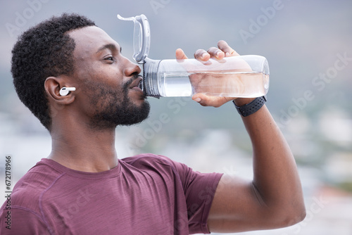 Fitness, drinking water and black man in outdoor nature for exercise, training and running with music, audio streaming service. Tired runner, sports or athlete man with water bottle for workout