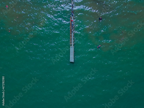 Aerial top down view of a wooden pier in the sea. Wooden pier and people. Pier of Rimini, Italia, Emilia-Romania. Top aerial view from drone to seascape. Natural marine background with waves.