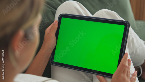 Girl click green screen. Hand hold horizontal ipad close up. Finger tap center tablet. View web store site. One touch chroma key pad. Woman poke display. Person work home room lie sofa. Social media. photo