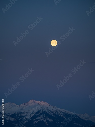 Snowy winter alpine landscape after sunset  pink purple sky with a full moon over a mountain peak