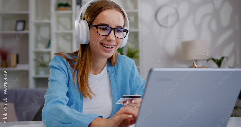 Young Caucasian business woman sitting at table holding credit card and using laptop for online shopping. Concept of online payment e-commerce, internet banking, spending money working from home Young Caucasian business woman sitting at table holding credit card and using laptop for online shopping. Concept of online payment e-commerce, internet banking, spending money working from home