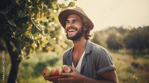 Young adult farmer holding fresh apples, with a beautiful orchard nature landscape in the background, representing a wellbeing, joy, hard work and natural way of living