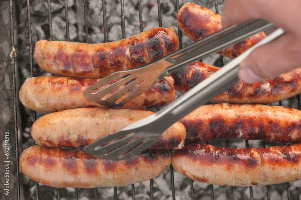 Grilled sausages. Cook man preparing grilling food bbq. Barbecue with smoke, flame outdoors. Tasty juicy german bratwurst. Charcoal kettle grill outside in backyard. Family summer vacation. Close-up