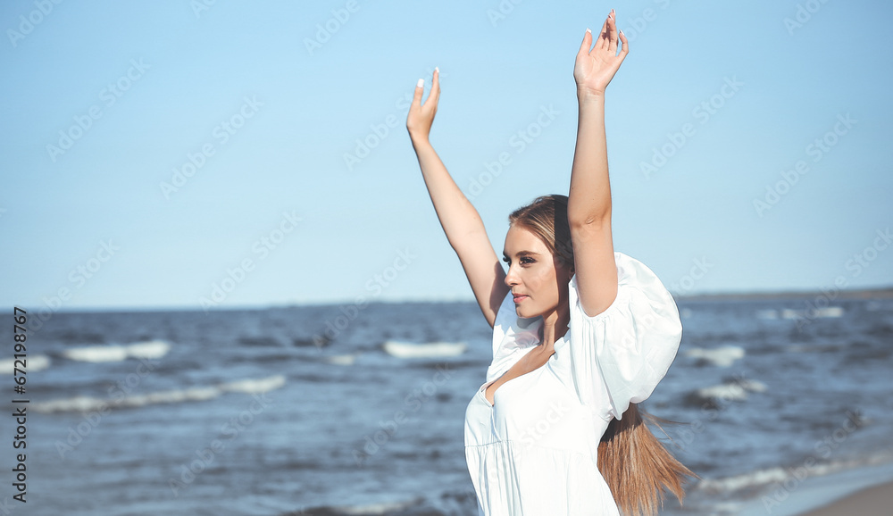 Happy smiling beautiful woman on the ocean beach standing in a white summer dress, raising hands Happy smiling beautiful woman on the ocean beach standing in a white summer dress, raising hands