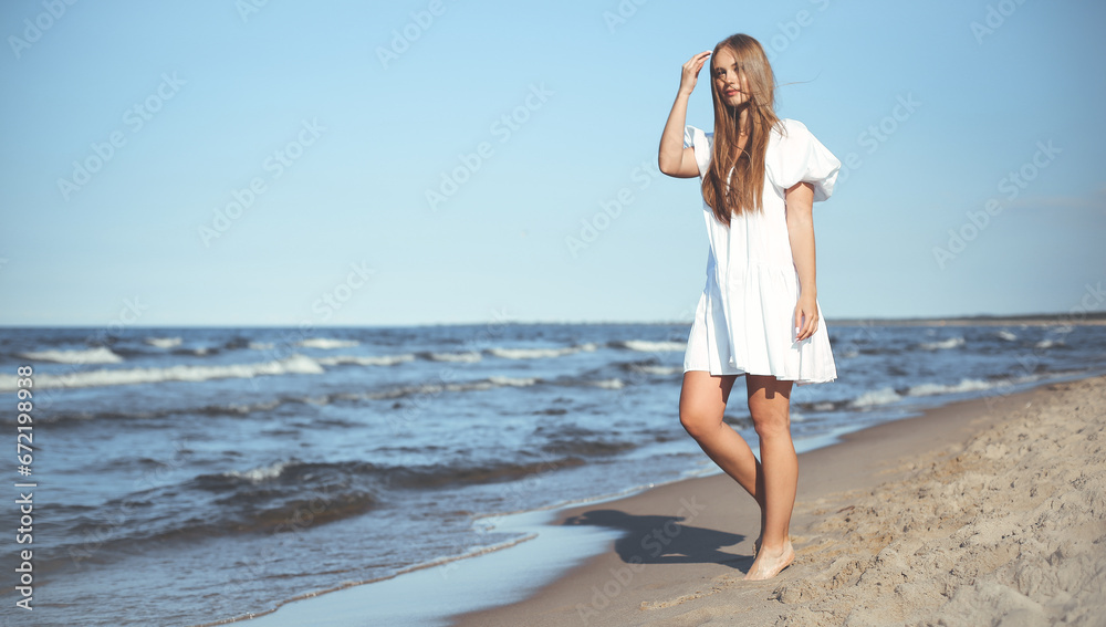 Happy smiling beautiful woman is walking on the ocean beach in a white summer dress Happy smiling beautiful woman is walking on the ocean beach in a white summer dress