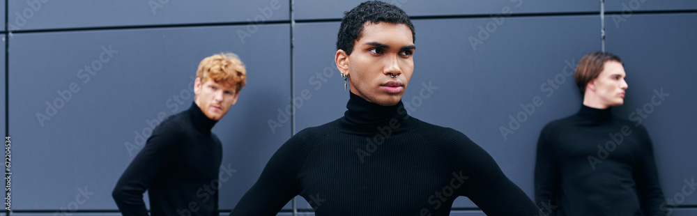 Obraz premium attractive african american man in turtleneck with earring posing in front of other men, banner