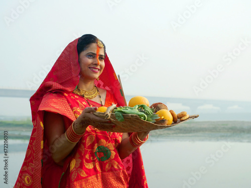 A woman offering prasad  fruits  vegetables  and other items and a Diya to pray sun God at a lake during Chhath Puja. Hindu devotees worship God sun with a ritual while standing in a river - Hindu ... photo