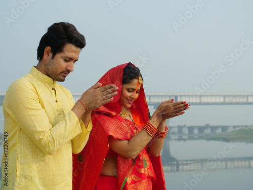 A couple worshipping Lord Sun at sunrise and celebrating the Chhath Pooja - auspicious day  Bihari family  Bihar. A man and a woman in chhath pooja attire praying to God Sun  celebrated in West Ben... photo
