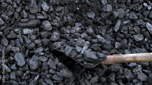 Worker takes black coal from a pile with a shovel. Energy industry. Solid fuel. Stove fireman at work.
