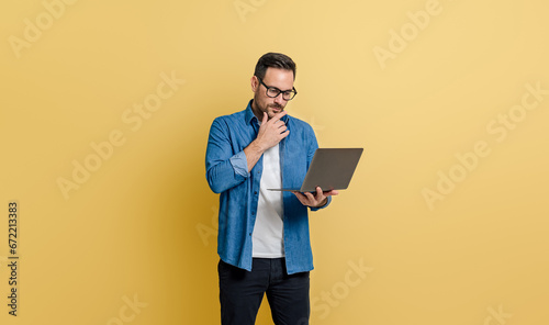 Canvastavla Focused young businessman touching chin and reading e-mails over laptop against