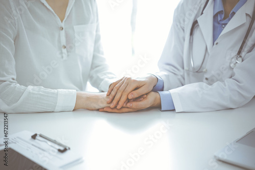 Doctor and patient sitting near each other at the table in clinic office. The focus is on female physician's hands reassuring woman, only hands, close up. Medicine concept
