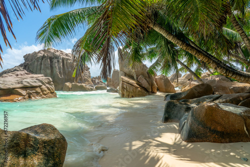 Granite rocks and palm trees on the scenic tropical sandy Anse Patates beach, La Digue island, Seychelles