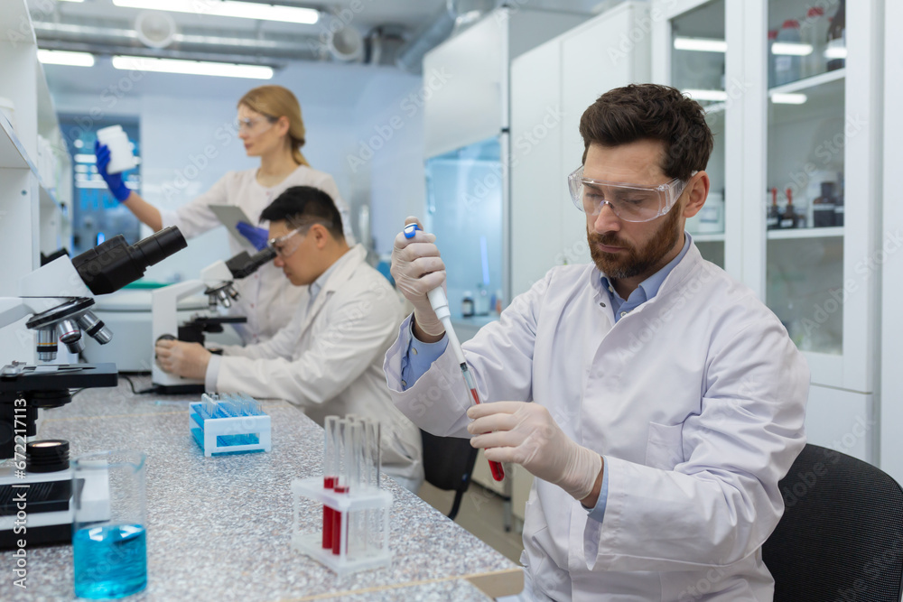 Fototapeta premium Mature serious and concentrated man works inside the laboratory, scientist conducts experiments examining the microscope.