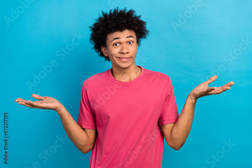 Portrait of funny guy dressed stylish t-shirt shrugging shoulders hands compare two products empty space isolated on blue color background photo