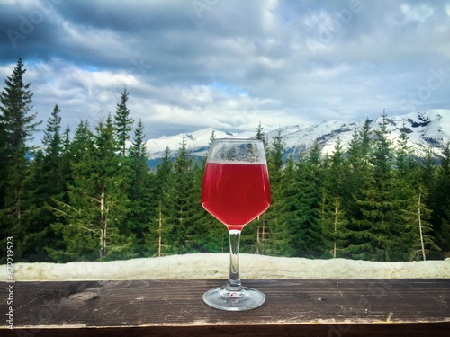 Glass of red wine placed with coniferous trees and snowcapped mountains in the background on a cloudy winter day photo