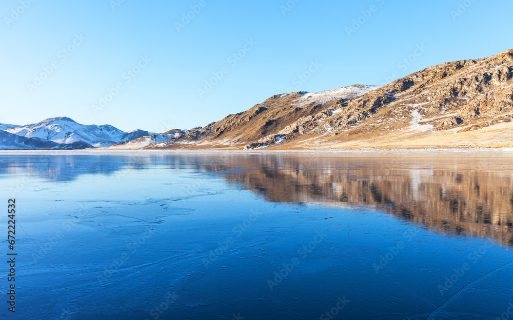 Baikal Lake during January freeze-up. View of clear fresh blue young ice with reflection of coastal hills at sunset. Winter scenic landscape. Natural cold background. Ice travel and outdoor recreation