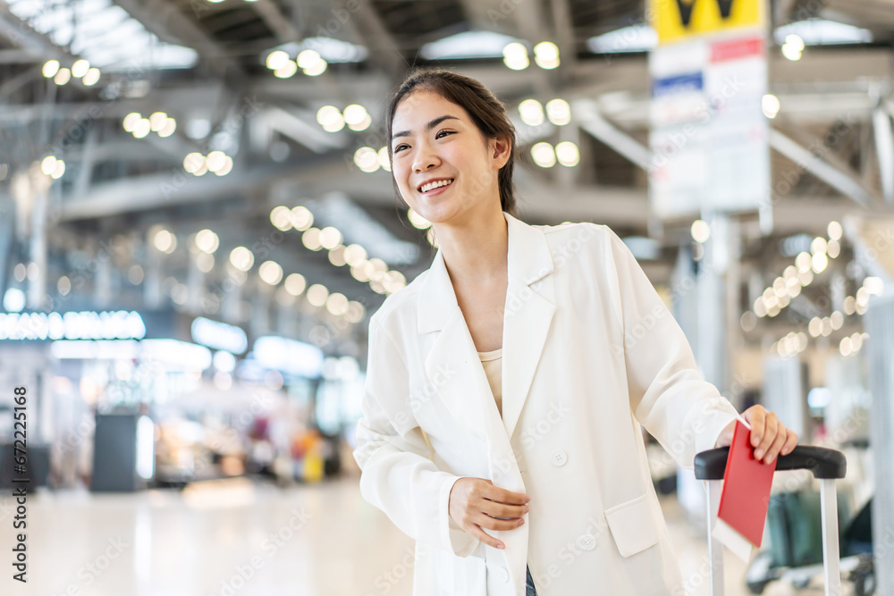 side view of young asian travel woman standing in airport waiting for flight. beautiful girl with backpack and luggages in hall of lounge area looking out friends