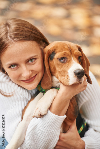 Sitting, holding animal and looking into the camera. Young woman is with her dog in the park © standret
