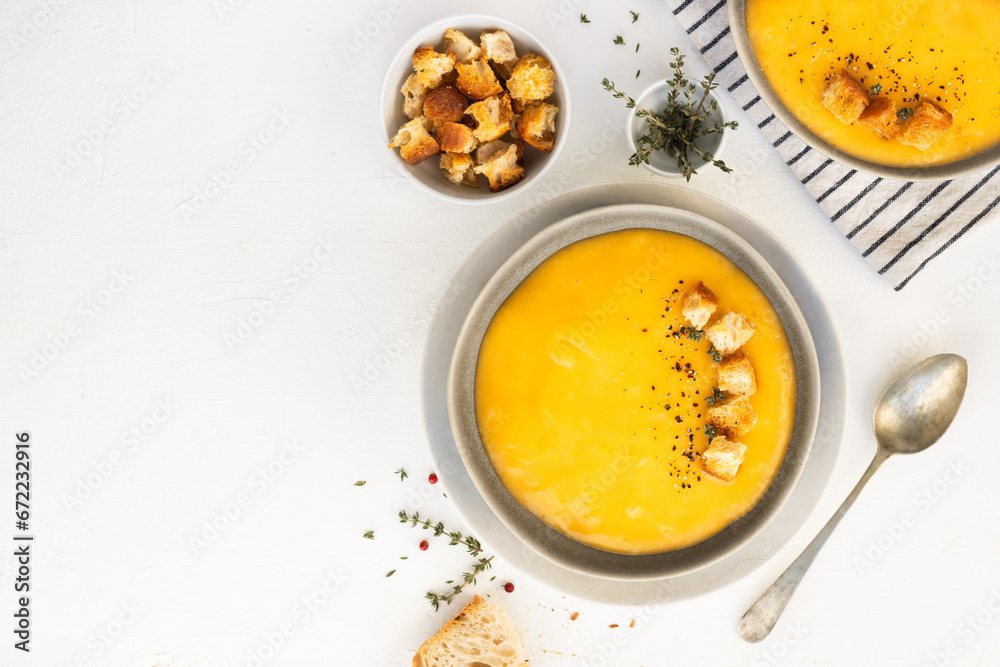 Bowl of pumpkin or vegetarian cream soup decorated with fresh rosemary, olive oil and croutons, on white textured background. Top view, copy space. square image Bowl of pumpkin or vegetarian cream soup decorated with fresh rosemary, olive oil and croutons, on white textured background. Top view, copy space. square image