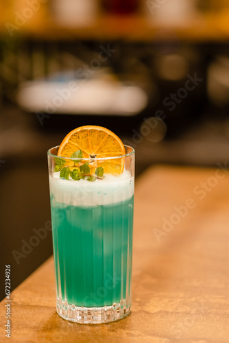  Side view blue curacao in a transparent glass with an orange chip, ice and thyme on bar counter in a restaurant, pub.