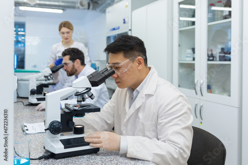 Serious thinking asian scientist working with microscope inside laboratory, man in white medical coat scientist working on sample research.