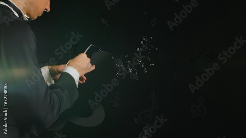 Close up on a black background stands a young man in a tuxedo, holding a wand in his hands. Depicts a conductor with a baton from which notes are issued. Creates a magical, musical atmosphere