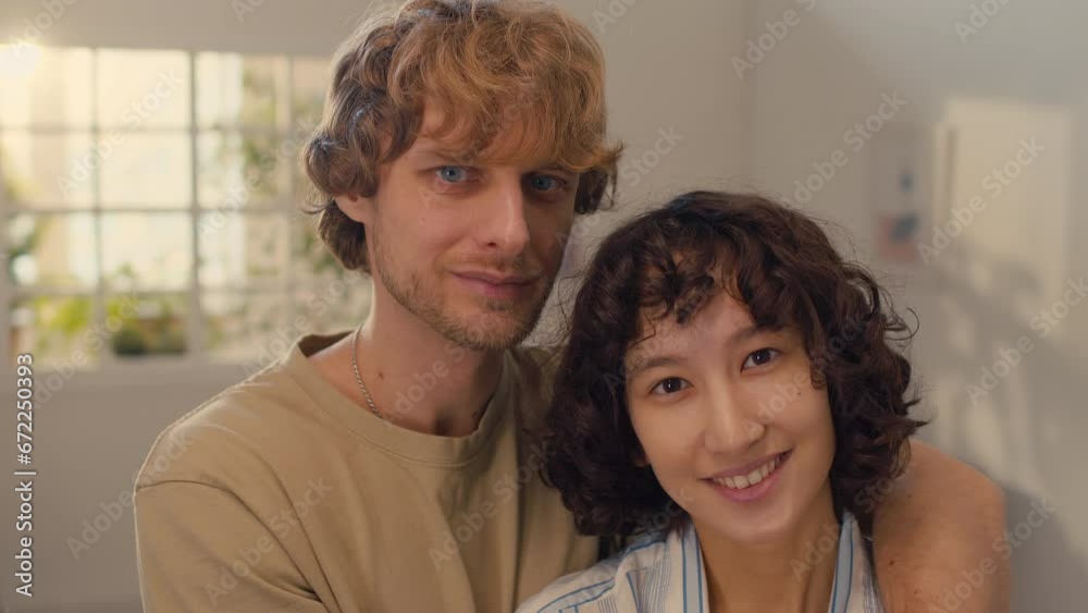 Close-up portrait shot of happy man and woman embracing each other while standing in well-lit room and looking straight at camera Close-up portrait shot of happy man and woman embracing each other while standing in well-lit room and looking straight at camera