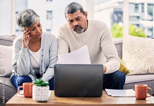 Documents, stress and senior couple on computer with finance paperwork, taxes or retirement research at home. Planning, debt and elderly people on sofa reading insurance, bills and asset management