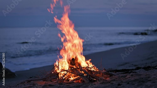 A campfire burns on a deserted sandy beach at the seashore in the evening