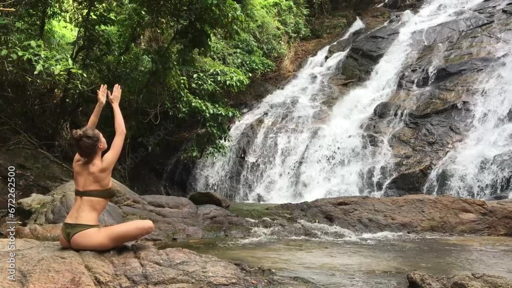 Woman doing sun salutation movements from yoga in front of waterfall Woman doing sun salutation movements from yoga in front of waterfall
