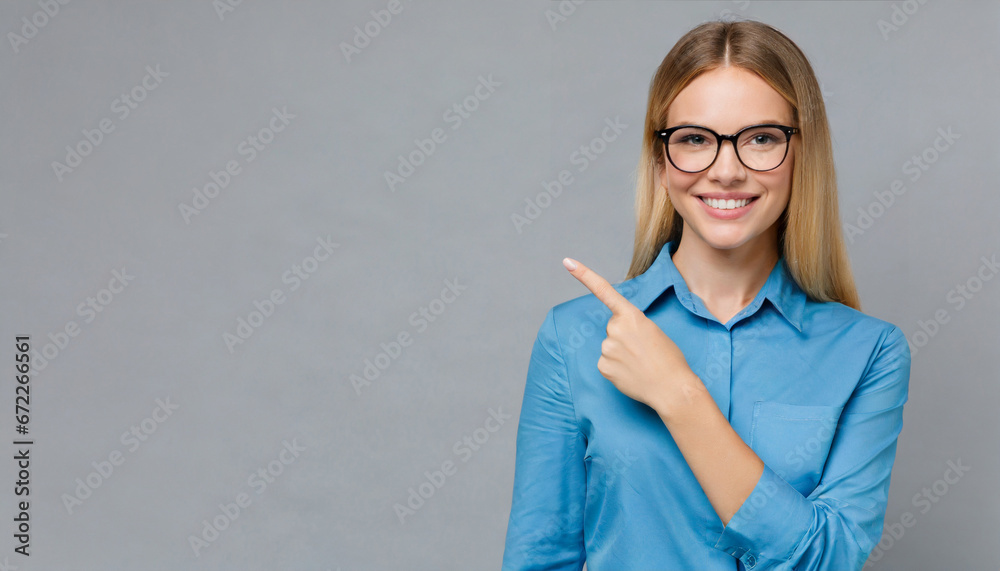 Happy young smiling professional business woman wearing blue shirt looking at camera pointing finger away at copy space showing aside presenting advertising offer standing isolated at gray background - obrazy, fototapety, plakaty 