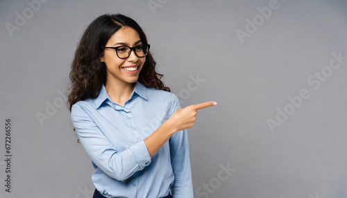 Happy young smiling professional business woman wearing blue shirt looking at camera pointing finger away at copy space showing aside presenting advertising offer standing isolated at gray background photo