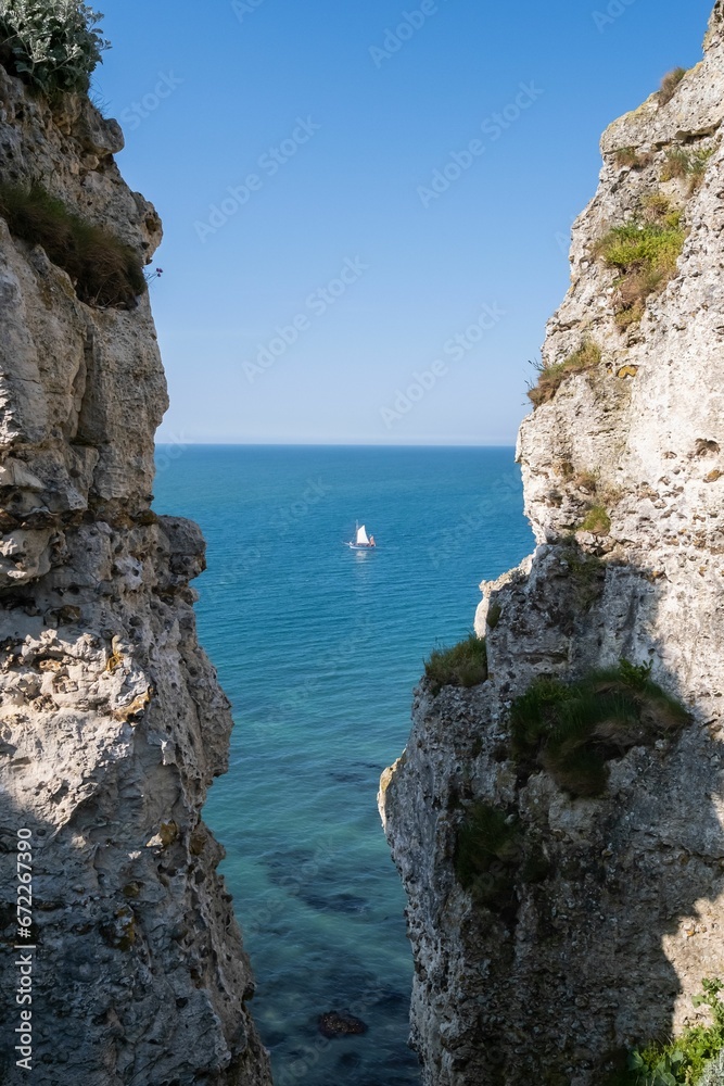 Fototapeta premium Sailboat is sailing in the ocean with cliffs in the foreground