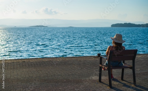 girl sitting on a bench on the pier at the sea and reflects © evacasasx