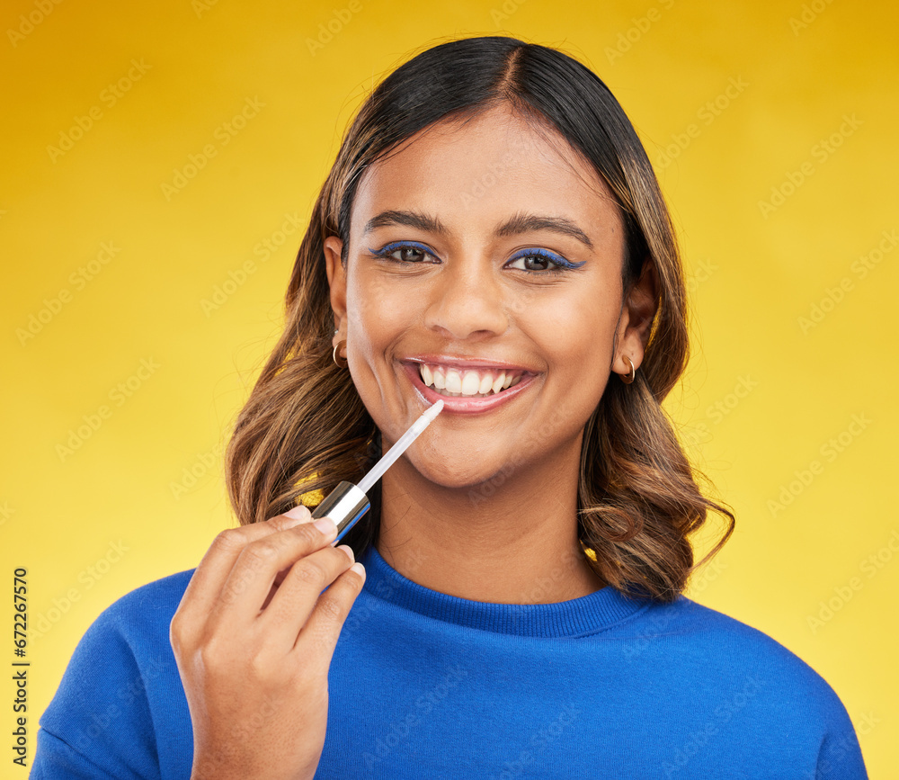 Woman, lip gloss and portrait of makeup in studio for beauty, glow and smile for cosmetics on yellow background. Face of happy indian model with lipstick product for facial aesthetics, shine and care - obrazy, fototapety, plakaty 